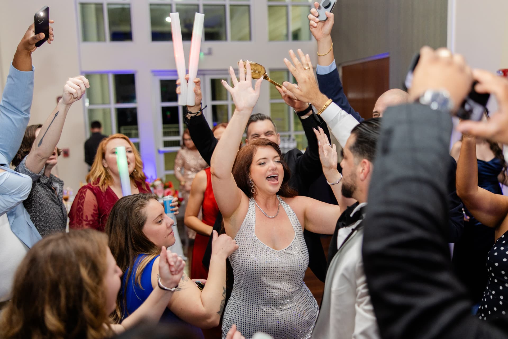 Wedding guests dancing and cheering with glow sticks during a high-energy reception