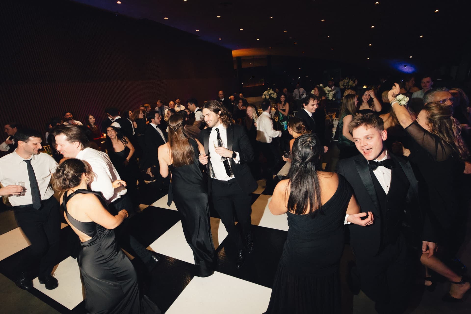 A packed wedding dance floor with guests dancing under stage lighting